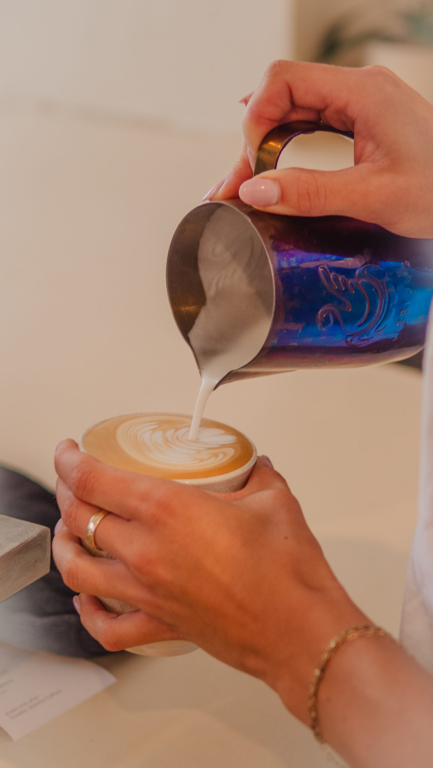 Hands pouring steamed milk into a latte, creating intricate latte art, with a focus on the coffee experience at Sunday Coffee.